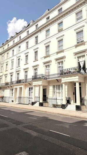 A row of white townhouses with multiple windows and balconies, a sidewalk in front, and a clear sky. - Cozy London Apartment With City Views (London)