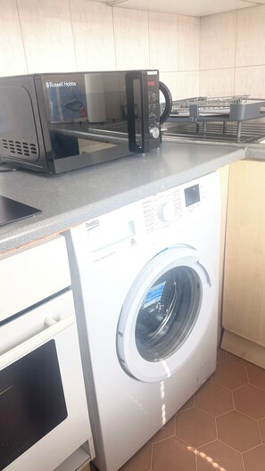 A kitchen with a microwave, a washing machine, and a kettle. - Cozy London Apartment With City Views (London)
