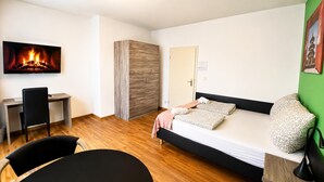 Una habitación moderna con cama, escritorio, silla y televisión que muestra una chimenea.