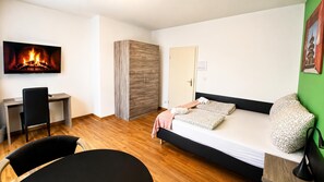 Una habitación moderna con cama, escritorio, silla y televisión que muestra una chimenea.