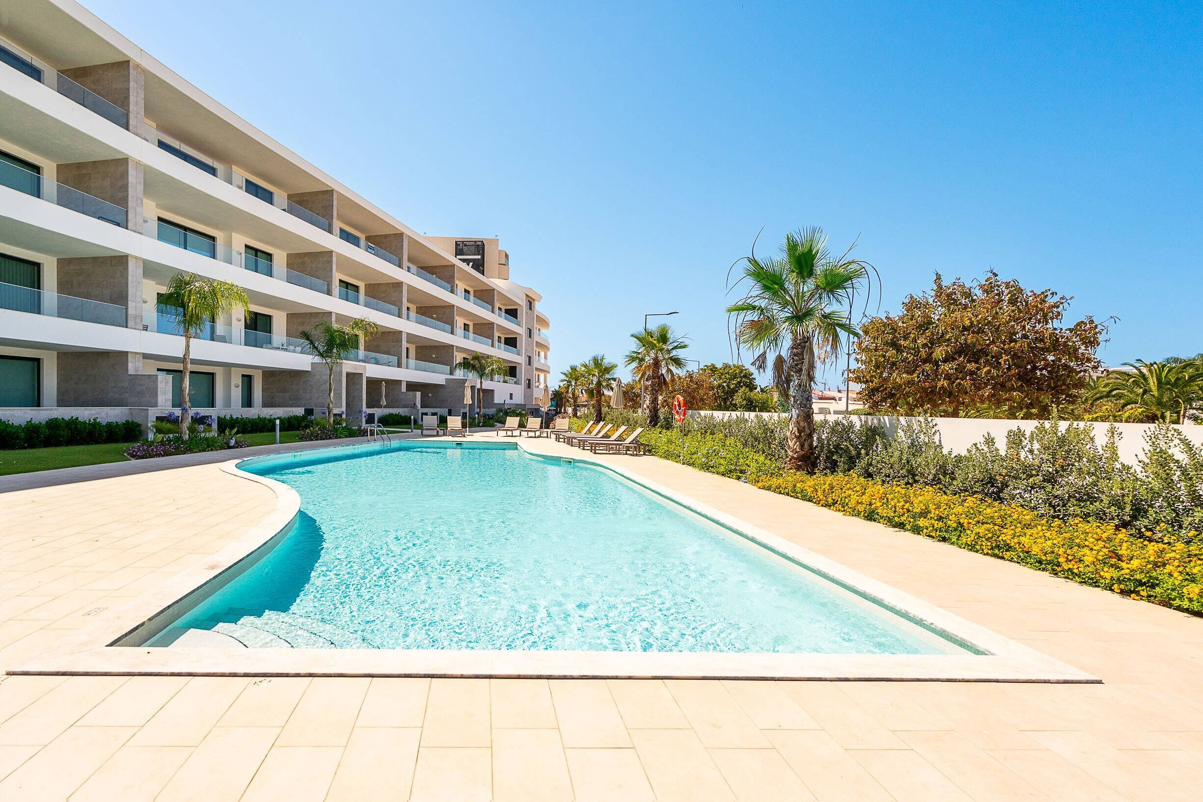 Ein modernes Hotel mit Schwimmbad, mehreren Balkonen und tropischer Bepflanzung.