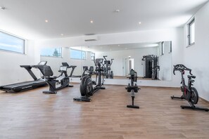Ein modernes Fitnessstudio mit unterschiedlichen Trainingsgeräten, großen Fenstern und Holzboden.
