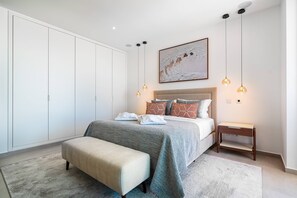 Ein Schlafzimmer mit Bett, Nachttisch, Bank und Schrank, sowie einem Kunstwerk an der Wand.