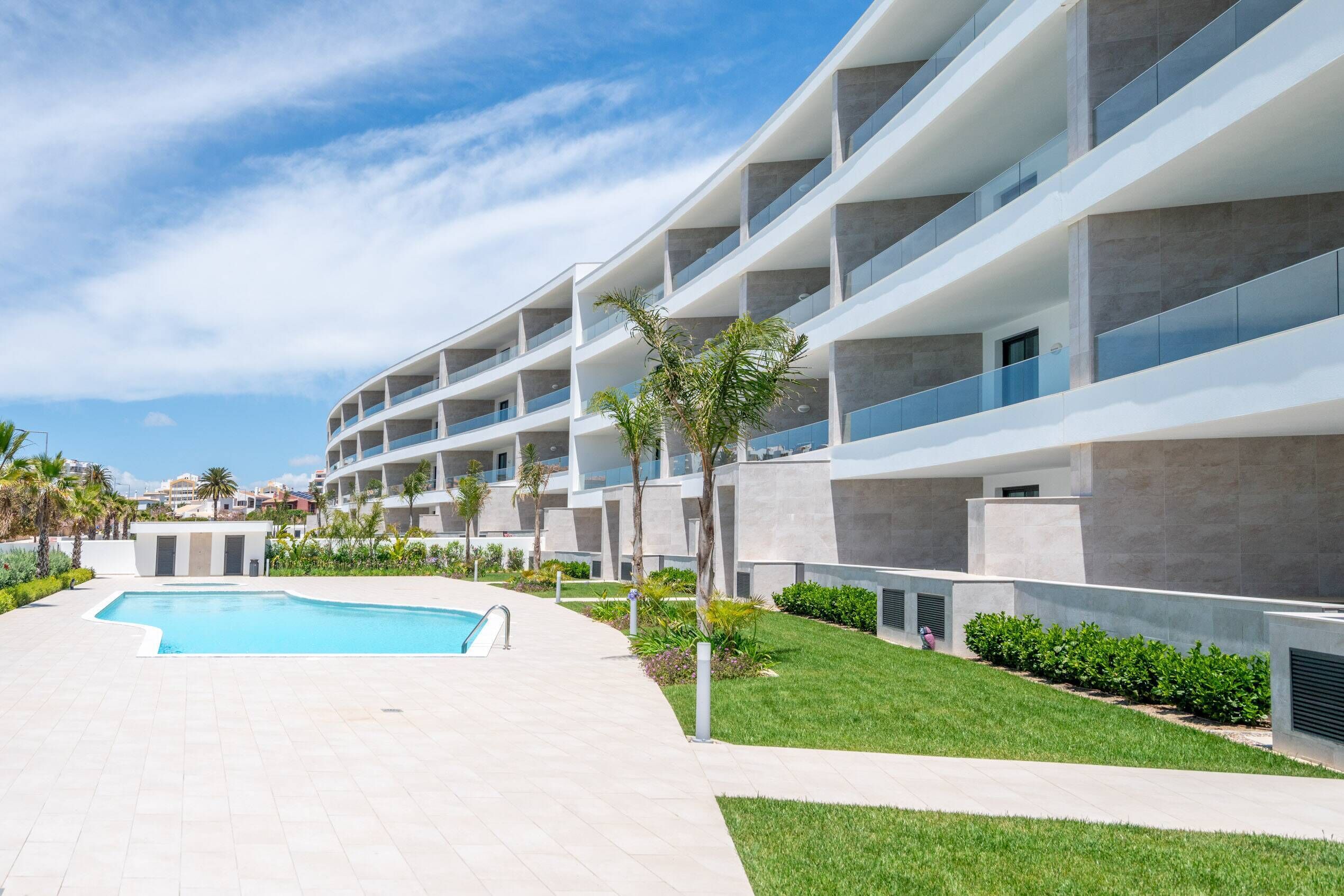 A modern hotel with multiple balconies, a swimming pool, and landscaped gardens.
