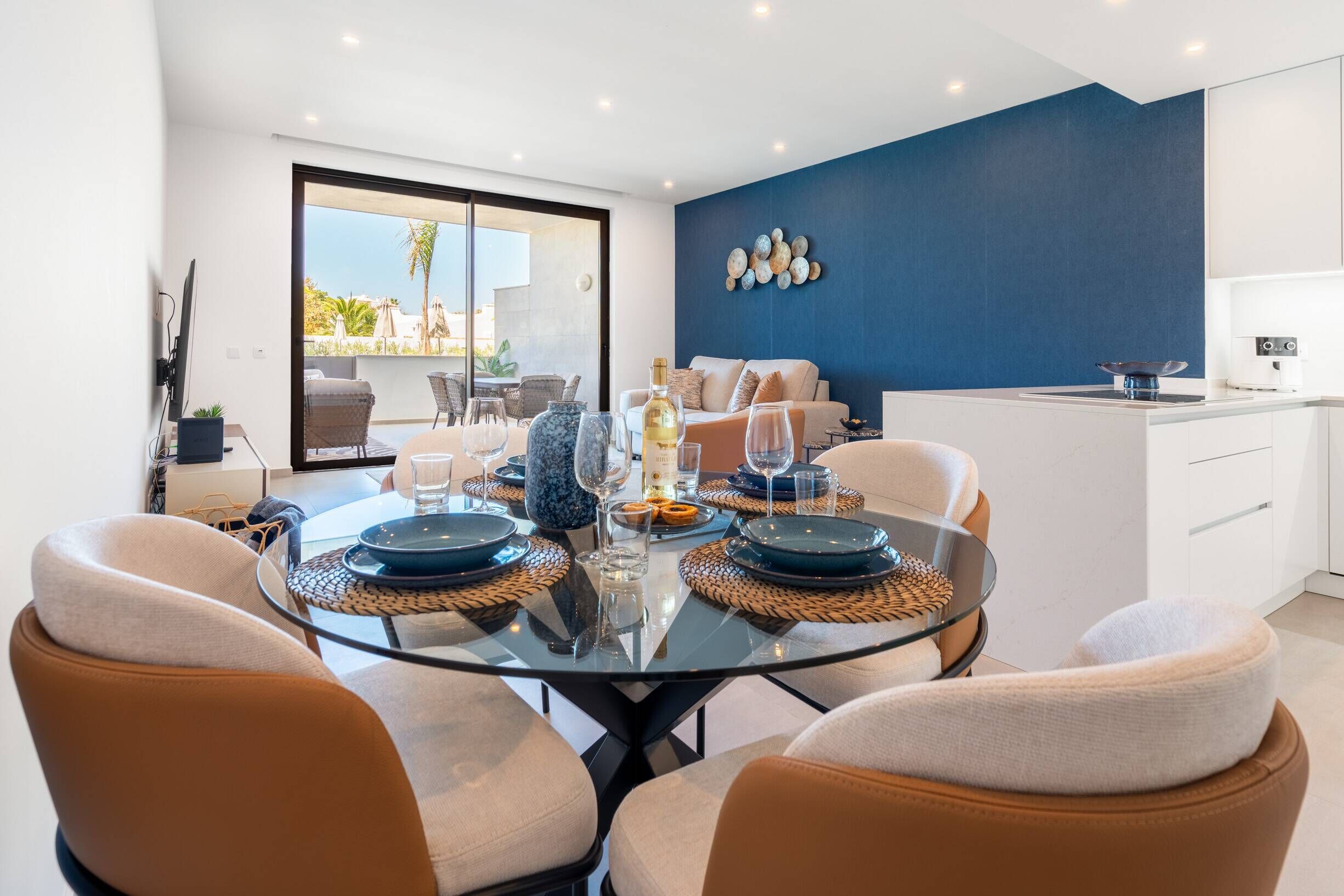 A modern dining area with a glass table, four chairs, and a view of the outdoors.