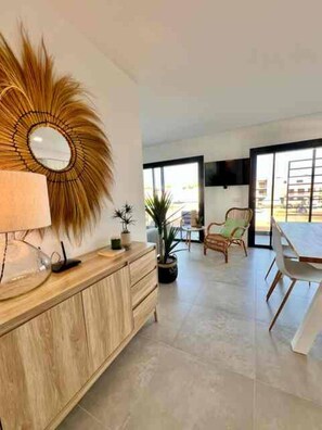 A modern living room with a wooden cabinet, a large mirror, and a dining area with chairs and a table. - Cabanas de Tavira - Sunrise Vibes (Tavira)