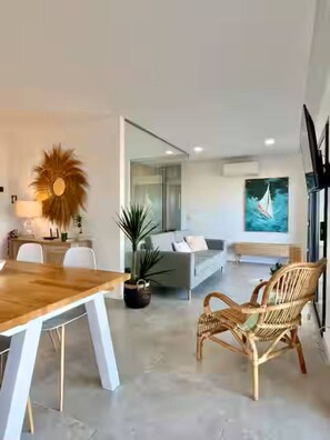 A modern living space with a dining area, a sofa, and a large window. - Cabanas de Tavira - Sunrise Vibes (Tavira)