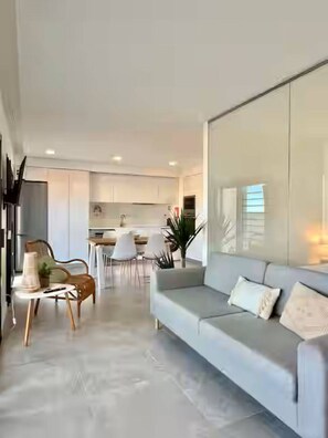 A modern living room with a grey sofa, a coffee table, and a dining area with white chairs. - Cabanas de Tavira - Sunrise Vibes (Tavira)