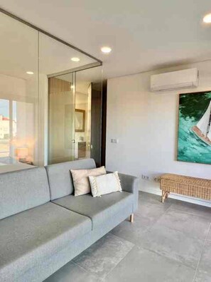 A modern living room with a grey sofa, a large painting, and a wicker bench. - Cabanas de Tavira - Sunrise Vibes (Tavira)