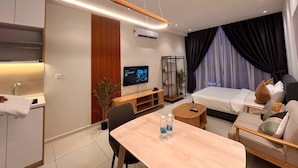 Moderni hotellihuone, jossa on puinen ruokapöytä, sohva, mustalla päätyosalla varustettu sänky, televisio ja ilmastointilaite.