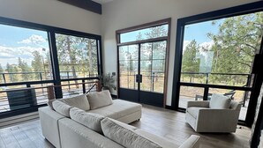 A spacious living area with a large sectional sofa, a smaller sofa, and a coffee table. The room features large windows offering a view of the outdoors. - Chelan Ridge (Chelan)