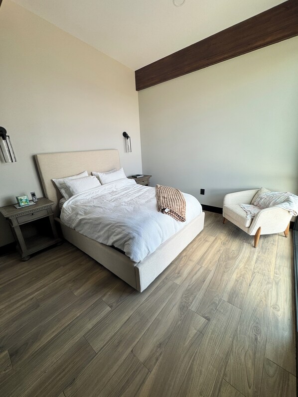 A bedroom with a bed, bedside tables, a nightstand, a chair, and a wooden floor.