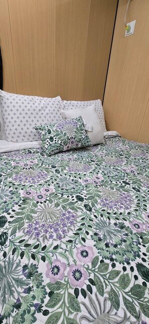 Een bed met een bloemenprintdeken, een wit kussen met een subtiel patroon, en een bijpassend kussen met een gedetailleerder ontwerp.