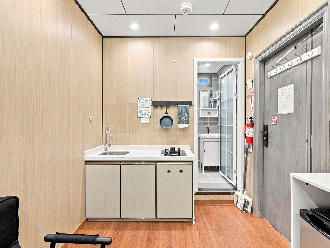 Una cocina moderna con un lavamanos, armarios y una estufa. Hay una puerta que da a un baño con ducha e inodoro.