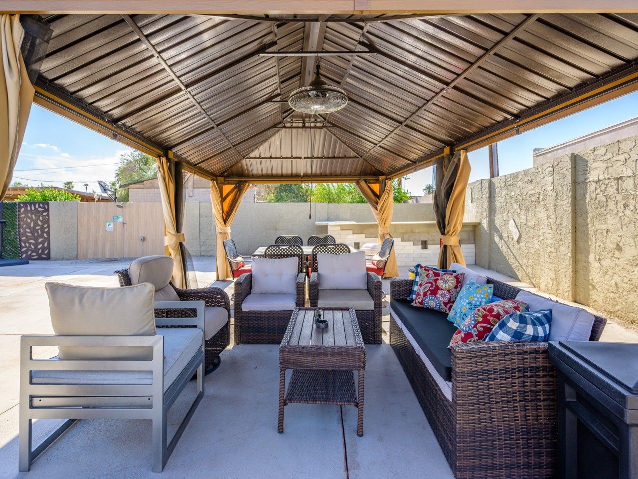 Un espace extérieur aménagé en terrasse, avec des meubles en osier, un ventilateur de plafond et une vue sur le quartier environnant.