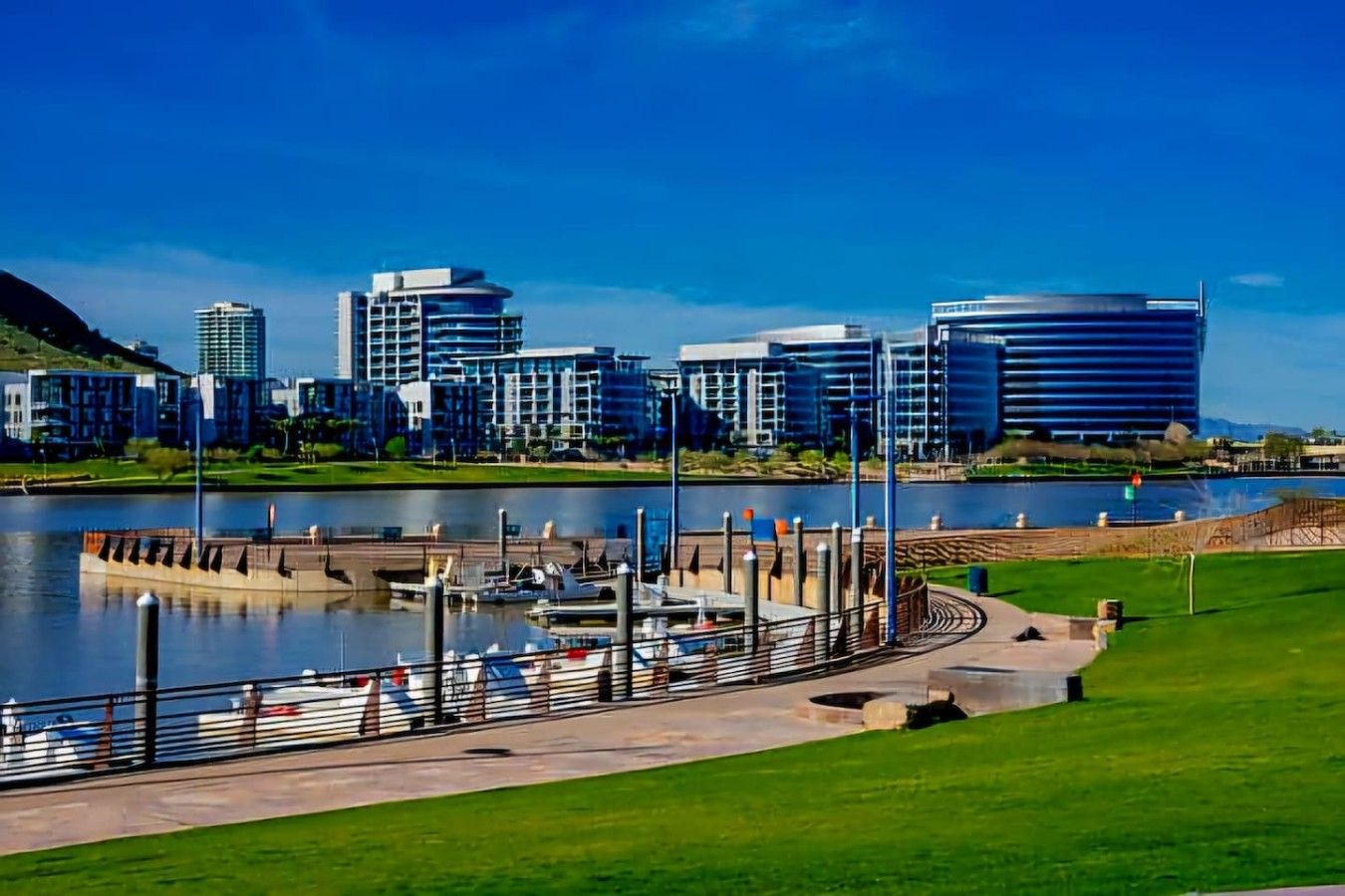 Un puerto deportivo con barcos amarrados, un paseo marítimo y edificios modernos al fondo.
