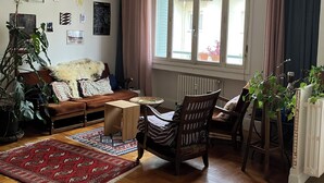 Ein Wohnzimmer mit einer Couch, einem Holzstuhl, einem Esstisch und einem großen Fenster mit Vorhängen.
