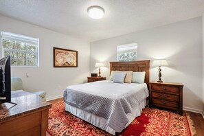 Ein Schlafzimmer mit einem Bett, Nachttischen, einem Fernseher, einem Fenster und einem Gemälde.