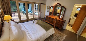 Ein Schlafzimmer mit Bett, Kommode, Spiegel und Blick ins Freie durch eine Glastür.