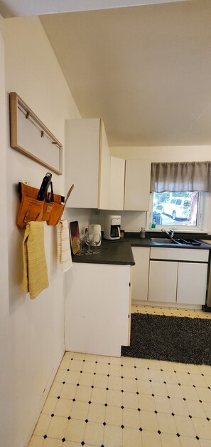 A compact kitchen with white cabinets, a coffee maker, and a window with a view of a car. - West Vancouver 5BR/4BA House | Patio · Garden & BBQ (West Vancouver)