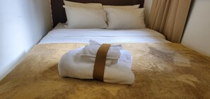 A neatly made bed with white linens and a brown towel with a brown strap on a textured brown bedspread. - West Vancouver 5BR/4BA House | Patio · Garden & BBQ (West Vancouver)