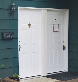 A white door with a brass knocker and a mail slot, a mailbox, and a welcome sign on a green wall. - West Vancouver 5BR/4BA House | Patio · Garden & BBQ (West Vancouver)