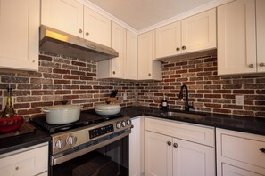 A kitchen with white cabinets, a brick backsplash, a stove, and a sink. - Welcome to Lewis Bay Celtic Cottage tucked on a quiet street close to the beach (Yarmouth)