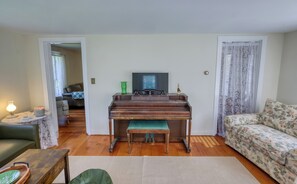 A living room with a piano, a sofa, a coffee table, and a television. - Welcome to Lewis Bay Celtic Cottage tucked on a quiet street close to the beach (Yarmouth)