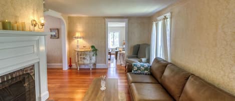 Uma sala de estar com lareira, um sofá, uma mesa de centro e um espaço de jantar ao fundo.