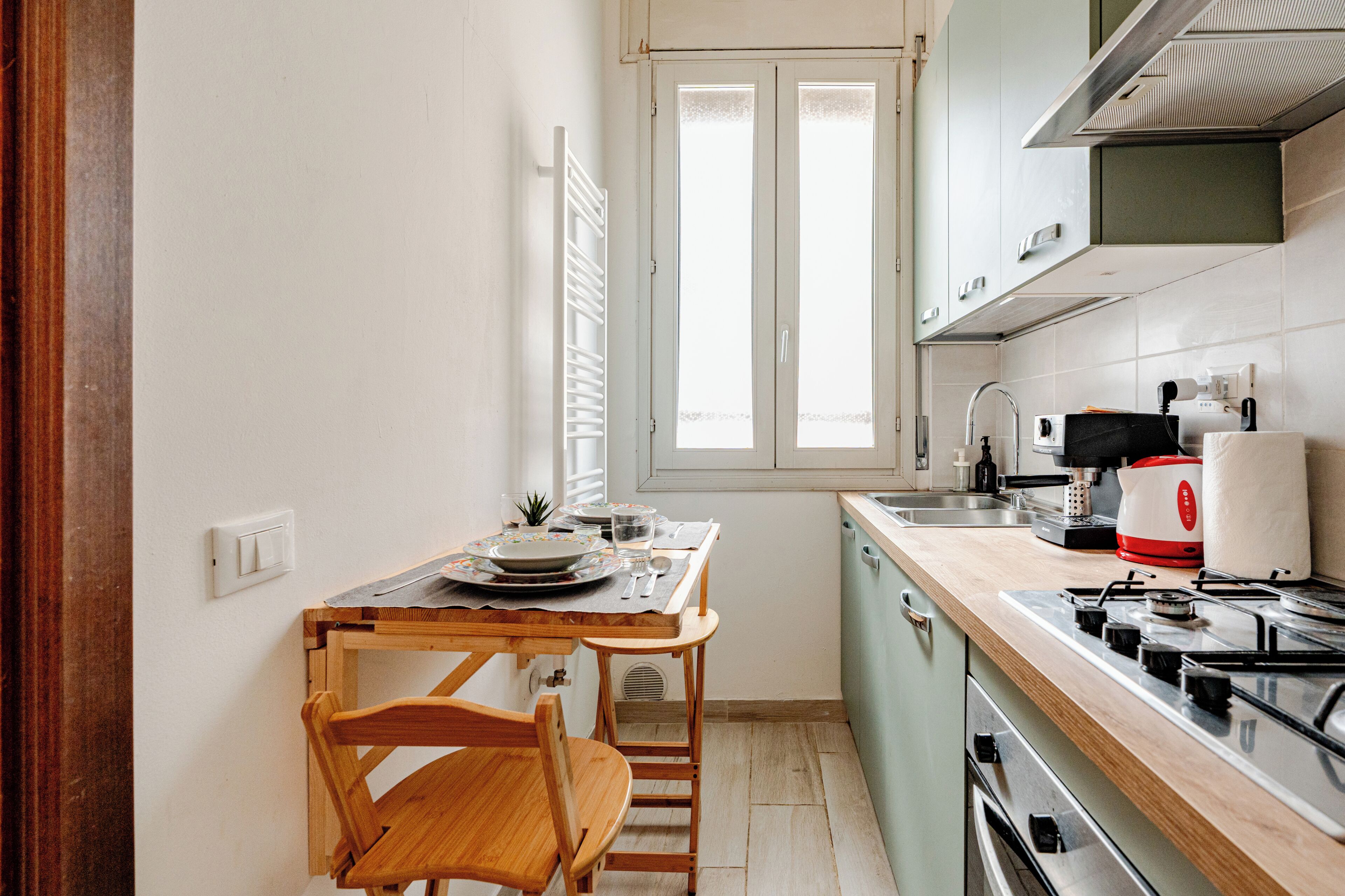 Cocina compacta con mesa, sillas, una ventana y electrodomésticos básicos.