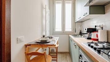 Cocina compacta con mesa, sillas, una ventana y electrodomésticos básicos.