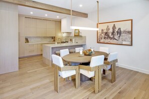 Eine moderne Küche mit Holzschränken, einer zentralen Kochinsel und einem Essbereich mit rundem Tisch und Stühlen.