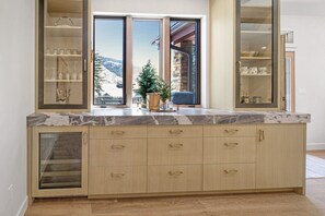 A kitchen with a marble countertop, wooden cabinets, and a view of a snowy landscape through large windows. - Modern Vail Townhome for Families & Friends - 3 Bed + Loft - Close to Bus (Vail)
