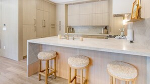 Eine moderne Küche mit Holzschränken, einer Marmorarbeitsplatte und drei Barhocker.