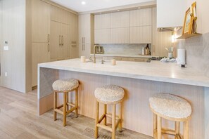Eine moderne Küche mit Holzschränken, einer Marmorarbeitsplatte und drei Barhocker.
