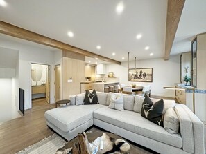 Ein modernes Wohnzimmer mit einem Ecksofa, einem Essbereich und einer Küche im Hintergrund.