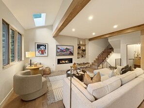 A modern living room with a fireplace, comfortable seating, a staircase, and a large window. - Modern Vail Townhome for Families & Friends - 3 Bed + Loft - Close to Bus (Vail)