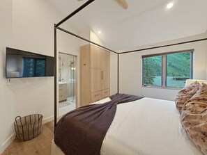 Ein modernes Schlafzimmer mit Bett, Fernseher, Fenster und Kleiderschrank.