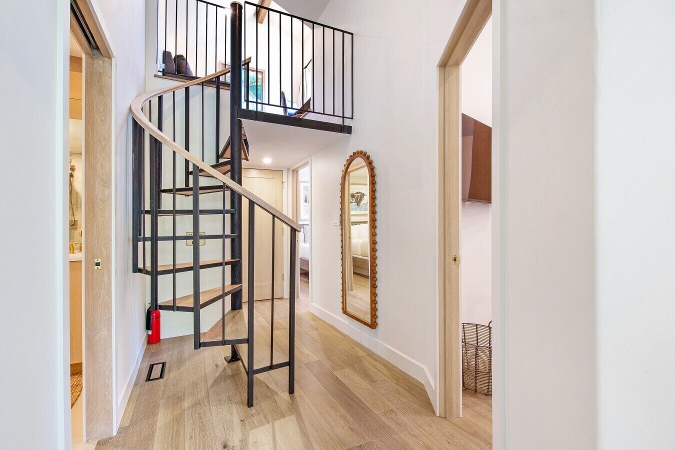 Un escalier avec une rampe noire menant à l’étage supérieur, un plancher en bois et un miroir accroché au mur.