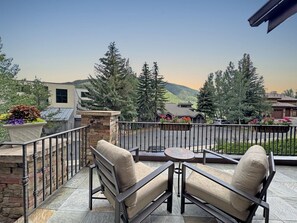 A balcony with outdoor seating, a view of trees and a distant mountain, and a stone wall. - Modern Vail Townhome for Families & Friends - 3 Bed + Loft - Close to Bus (Vail)