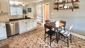 A kitchen with white cabinets, a stainless steel dishwasher, a granite countertop, and a dining area with a round table and chairs.