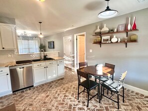 A kitchen with white cabinets, a stainless steel dishwasher, a granite countertop, and a dining area with a round table and chairs.