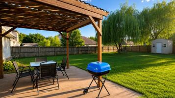 A covered patio area with a grill, outdoor seating, and a wooden pergola.