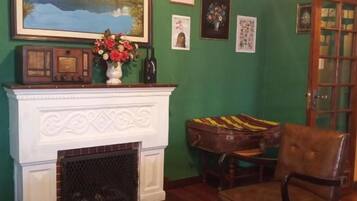 Una habitación con chimenea, una silla, una mesa y un cuadro en la pared.