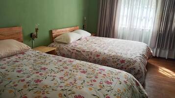 Un dormitorio con dos camas, paredes verdes y una ventana con cortinas.