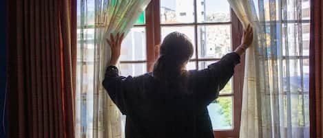 A person standing in front of a window with curtains, looking outside.