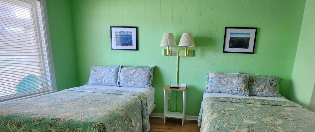 A room with two beds, a nightstand, a lamp, and two framed pictures on the wall.