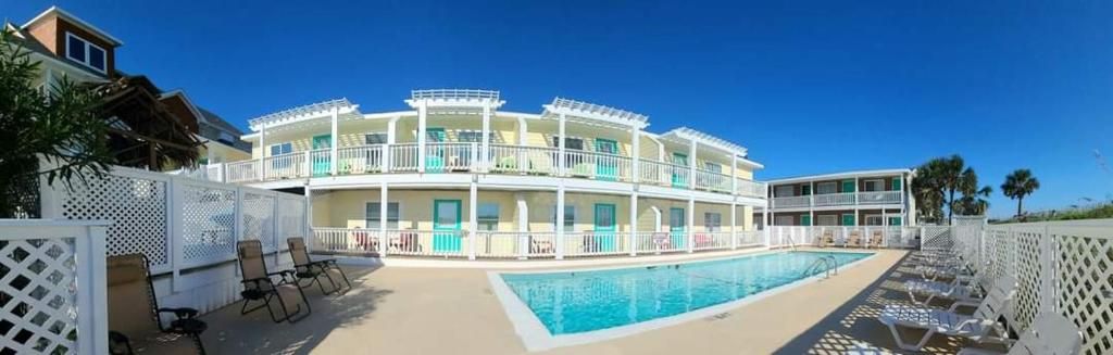 Um hotel com vários andares, área de piscina, espaço para sentar ao ar livre e cerca branca.