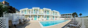 Un hotel de varios pisos con zona de piscina, mobiliario exterior y una valla blanca.