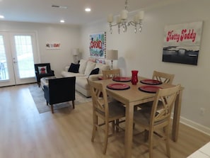A dining area with a wooden table set for four, a chandelier, and a 'Katty Todd' framed picture on the wall.